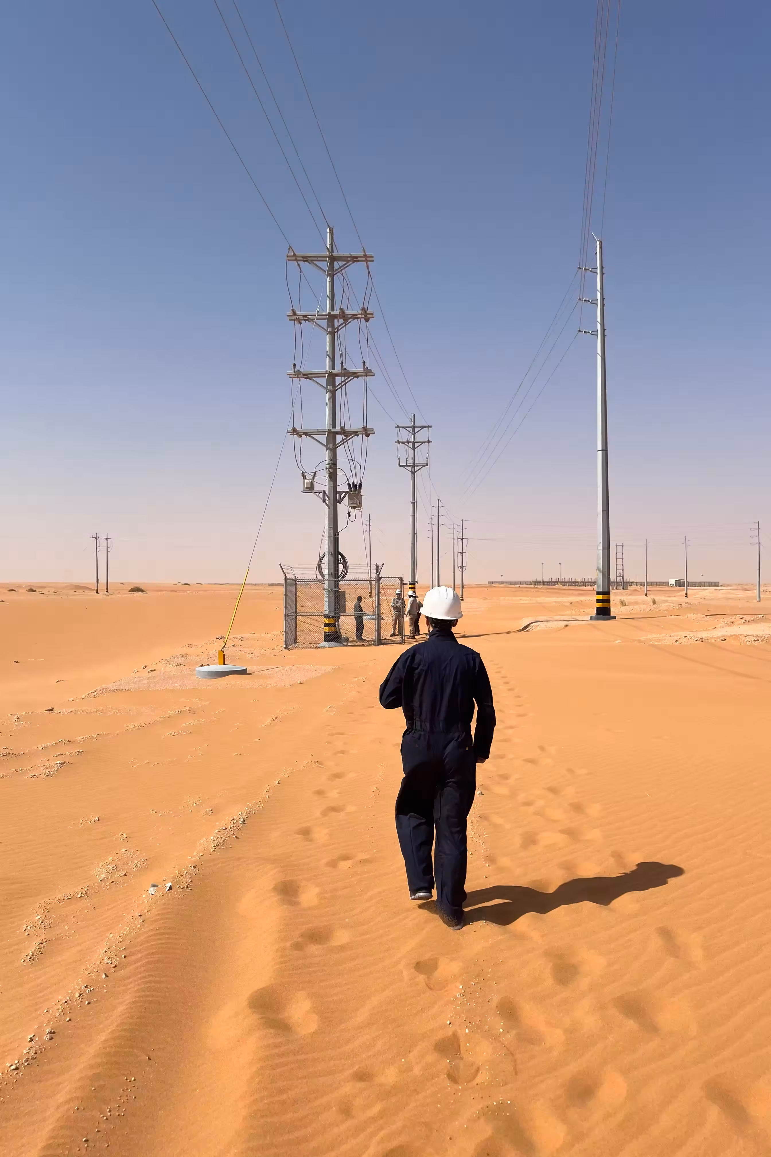 Worker walking towards power line in Arabian desert
